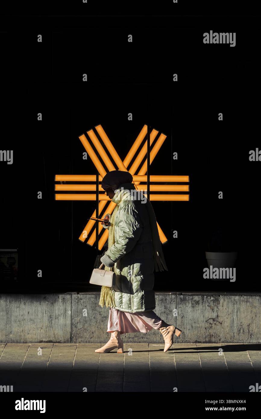 Una figura elegante passa davanti a un'installazione di luci geometriche che fonde la moda moderna con l'estetica urbana. Foto Stock