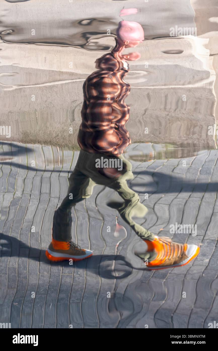 Un riflesso distorto di una persona che cammina, creando un effetto visivo surreale e astratto. Foto Stock
