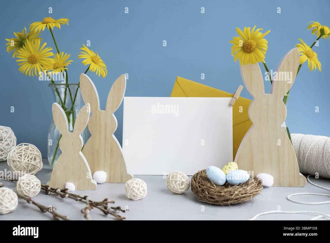 Spazio per le copie del biglietto di auguri per una busta bianca vuota con personaggi in legno e fiori freschi. Contenuto di composizione pasquale natura morta. Cr Foto Stock
