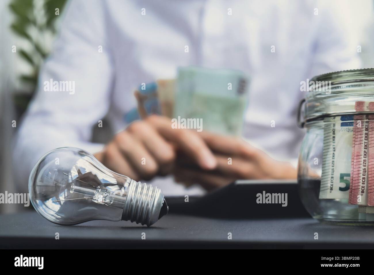Lampadina elettrica. Man Hands contabilizza le spese sulle banconote elettriche del contante in euro contante sul calcolatore. Primo piano di mani non riconoscibili Foto Stock