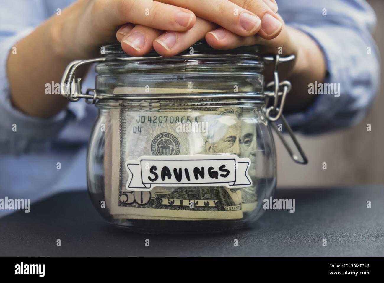 Donna irriconoscibile che tiene in mano denaro risparmiando in un barattolo di vetro pieno di banconote in dollari. Trascrizione DEI RISPARMI davanti al barattolo. Gestione delle finanze personali Foto Stock