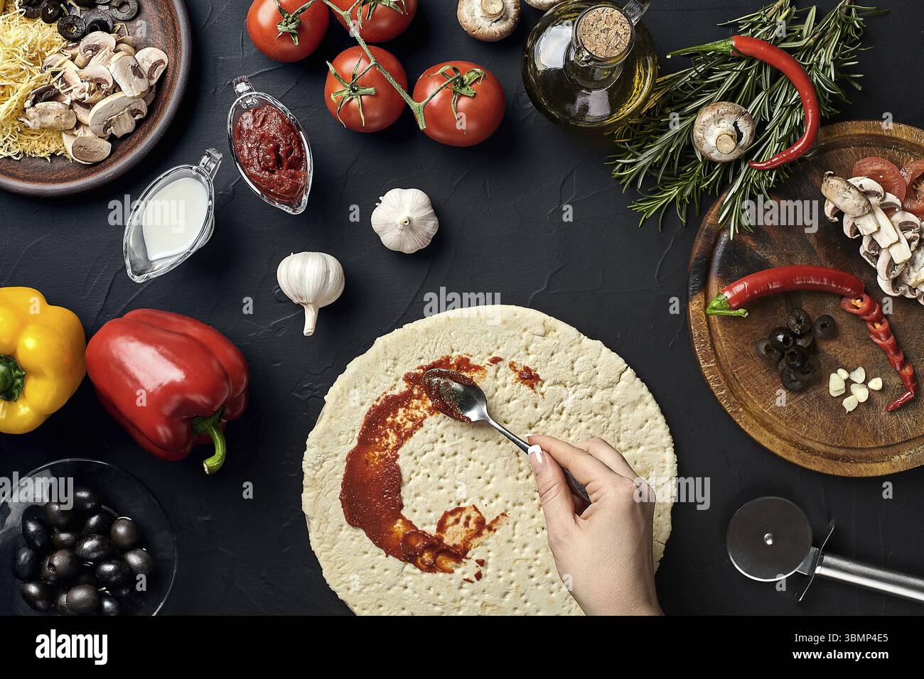 Mani di baker aggiunta di ingredienti in pizza pizza durante la preparazione in cucina. Funghi, pomodori, formaggio, cipolla, olio, pepe, sale, l'uovo, la grattugia o Foto Stock