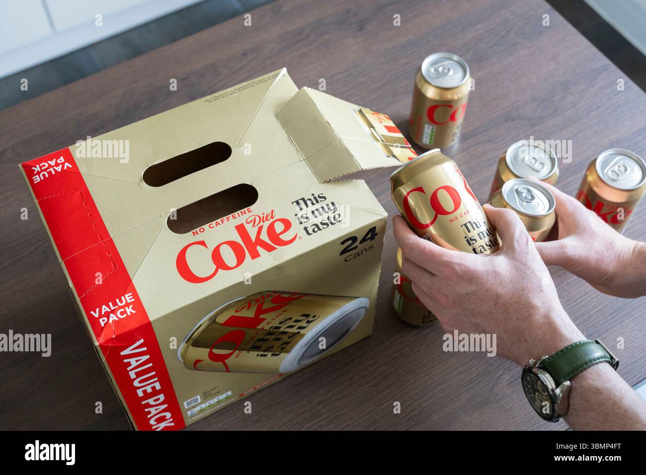 Mano che tiene senza caffeina lattine di coke dietetico e un pacchetto convenienza. La "tassa sullo zucchero" del Regno Unito (Soft Drinks Industry Levy SDIL) è una tassa sulle bevande zuccherate preconfezionate Foto Stock