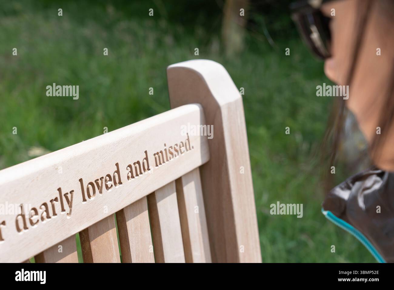 Una donna che guarda un messaggio inciso su una panchina di legno in un cimitero di una chiesa "amata e mancata", in Inghilterra. Concetto: Lutto, defunto Foto Stock