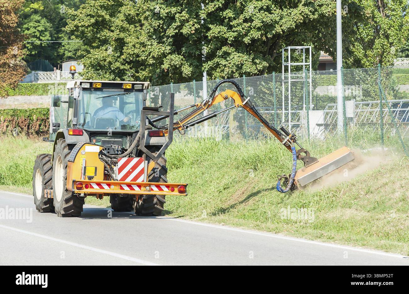 Manutenzione stradale. Tagliare l'erba sul ciglio della strada con il trattore Foto Stock