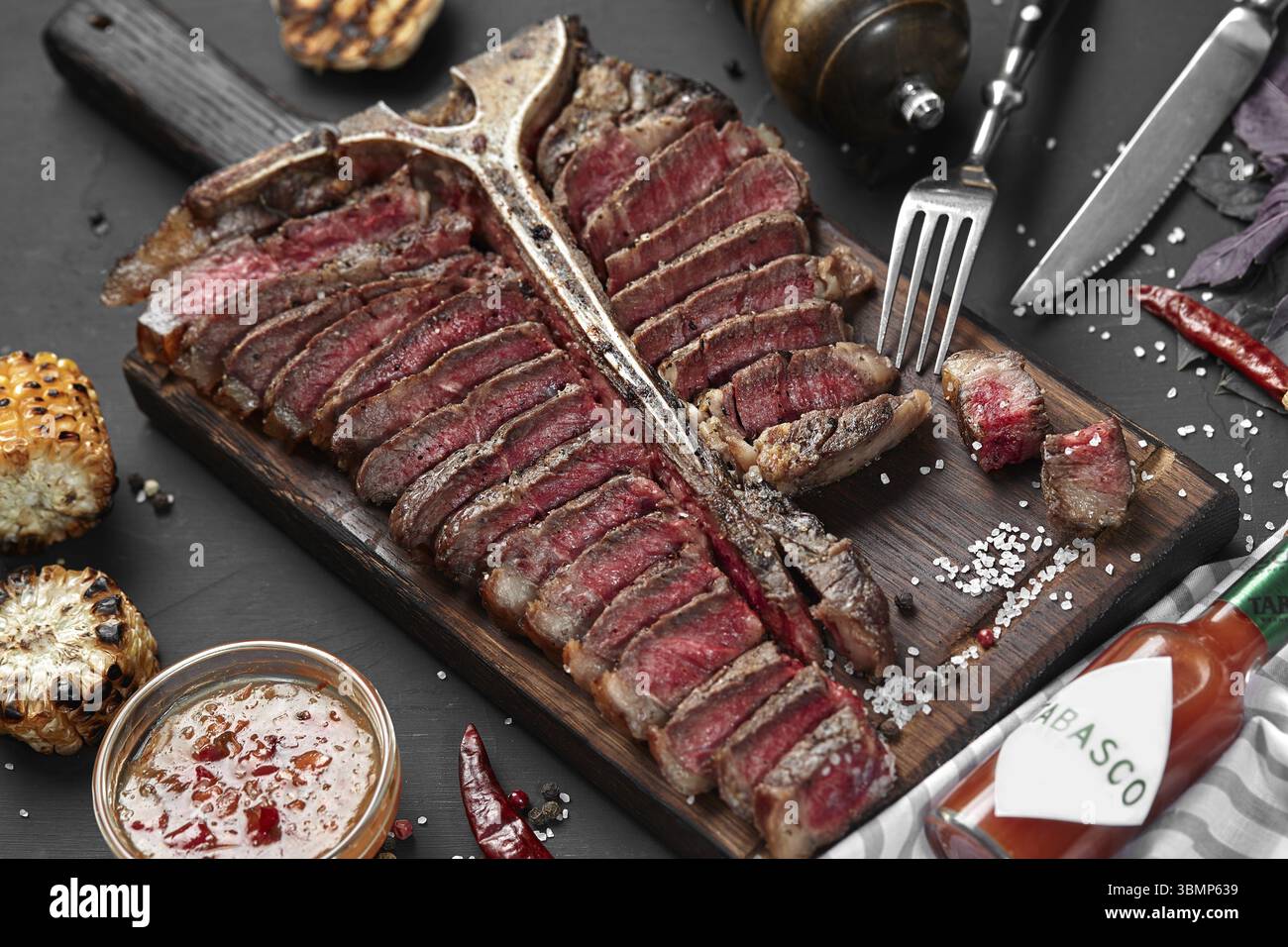 Tagliata T-bone giacente sulla tavola di legno. Grigliata di verdure in una padella grill. Sfondo nero. Close-up. Vista dall'alto. Still Life Foto Stock
