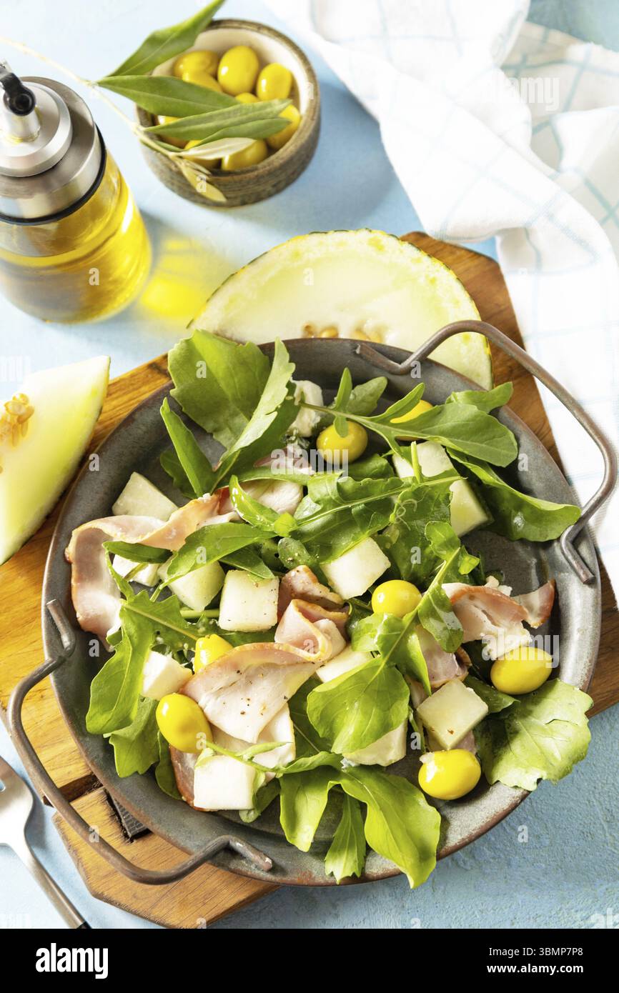 Antipasto tradizionale spagnolo e italiano. Insalata mediterranea estiva con melone, pancetta, olive, formaggio bianco e rucola su sfondo di pietra blu Foto Stock