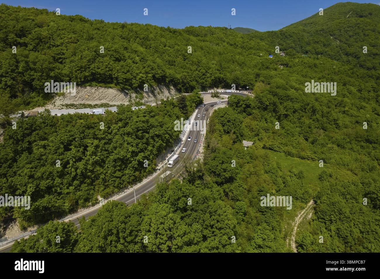 Vista aerea della strada tortuosa dall'alto passo di montagna. Ottimo viaggio in auto attraverso i fitti boschi. Vista a volo d'uccello Foto Stock