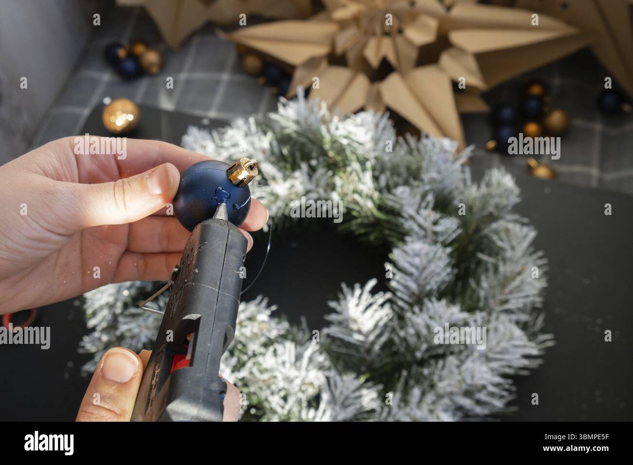 Artigiano con colla calda istruzioni passo dopo passo per realizzare una corona di Natale fatta a mano con decorazioni natalizie nei colori blu e giallo. Mano femminile Foto Stock