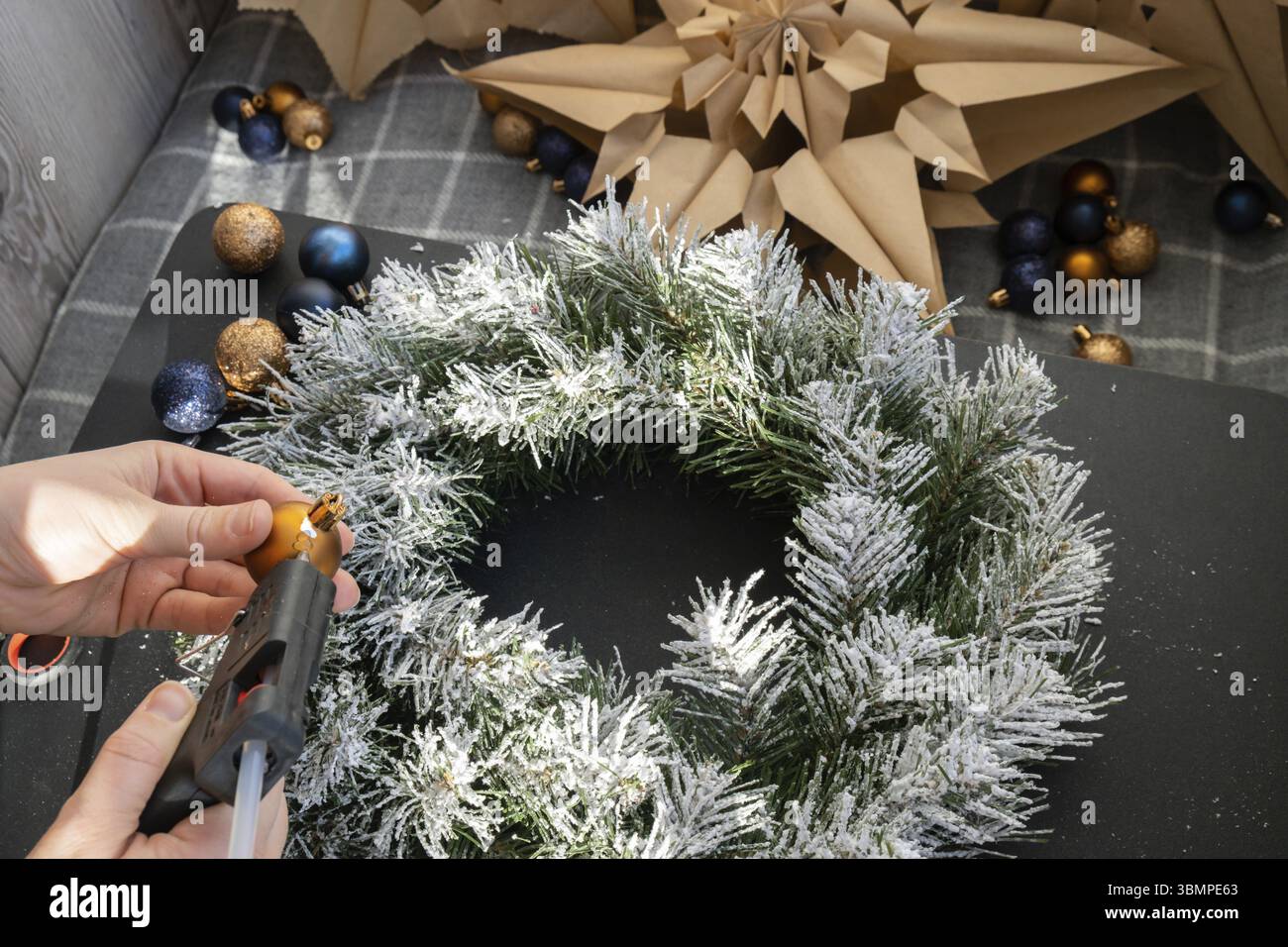 Crea usando colla calda la corona di Natale fatta a mano con decorazioni festose blu e gialle. Preparazione per le festività natalizie, master class di creatività Foto Stock