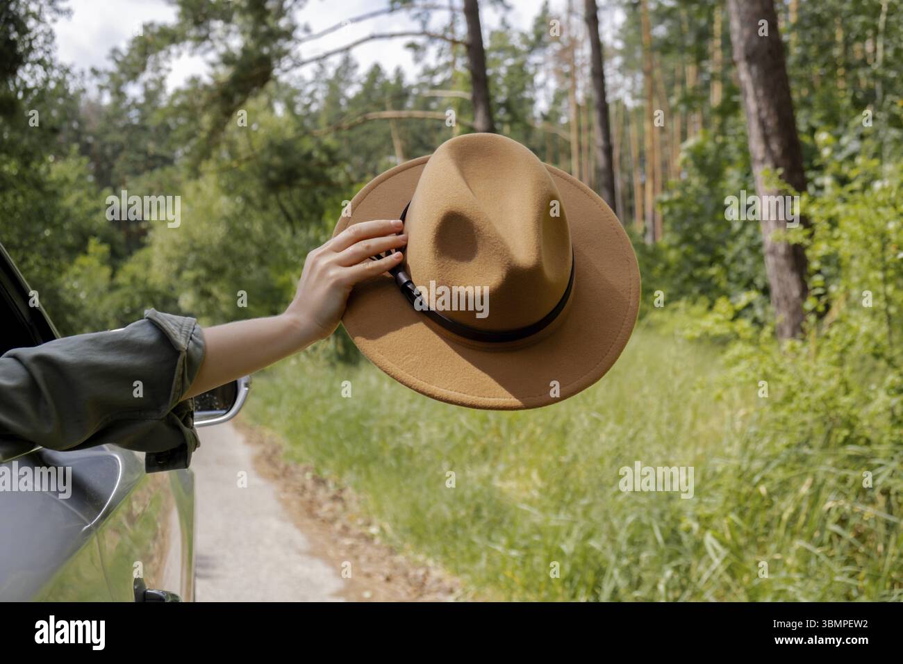 Donna che cavalca un'auto che tiene il cappello in mano fuori dal finestrino. Concetto di viaggio locale. Libertà e connessione con la natura. Un viaggio su strada per uno stile di vita sostenibile Foto Stock