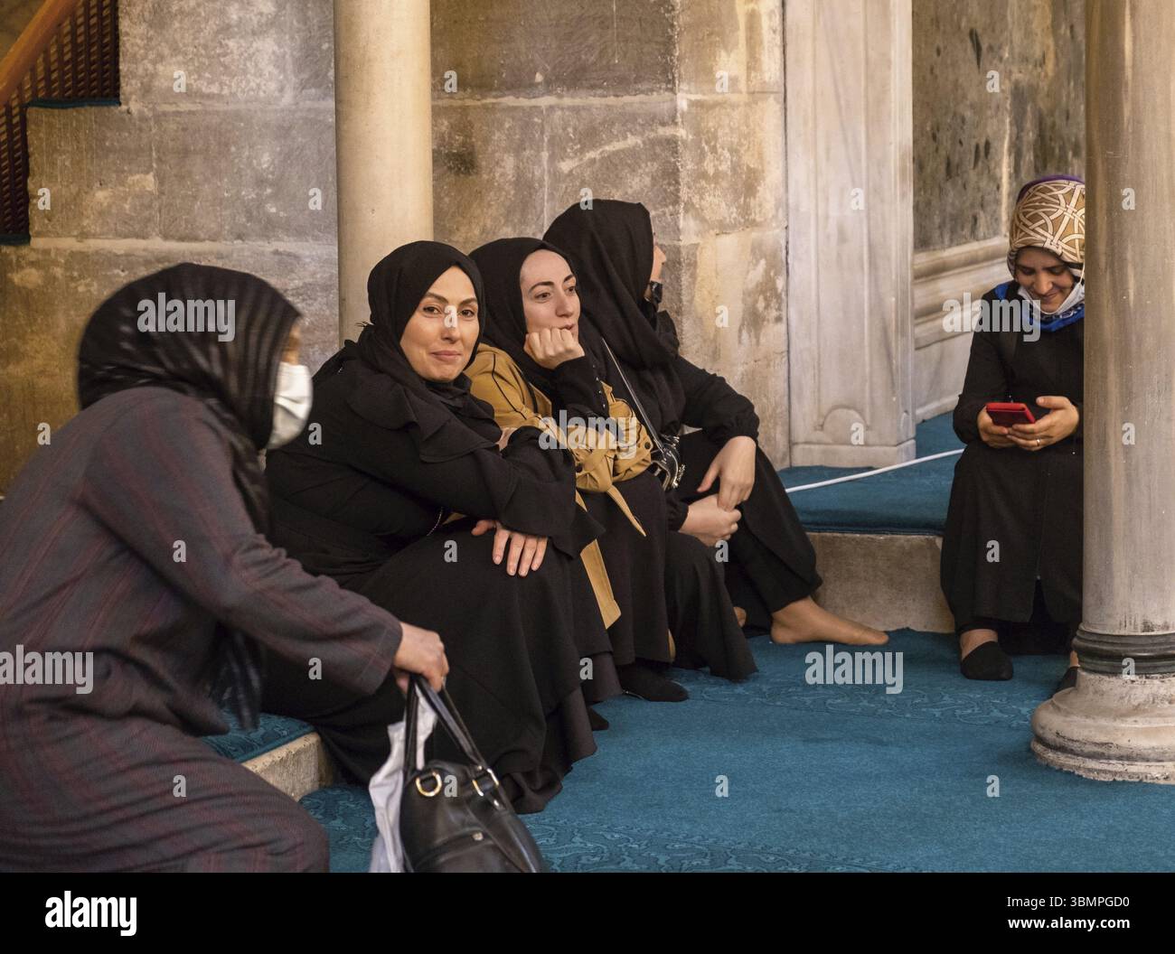 Gruppo di donne musulmane sedute e riposate in una moschea, una che usa il suo smartphone Foto Stock