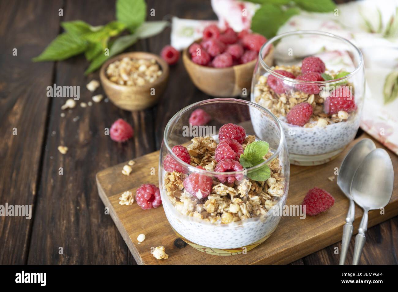 Menu della colazione salutare. Colazione di granola fatta in casa. Bicchiere di parfait di granola, lampone di bacche, yogurt con semi di chia su linguetta rustica Foto Stock