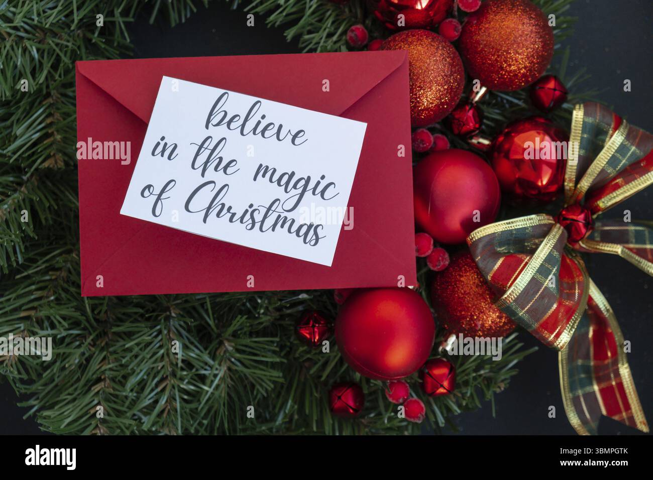 Corona di Natale fatta a mano con decorazioni natalizie con busta rossa e nota di carta con BELIEVE IN the MAGIC OF CHRISTMAS text. Vacanze invernali cel Foto Stock