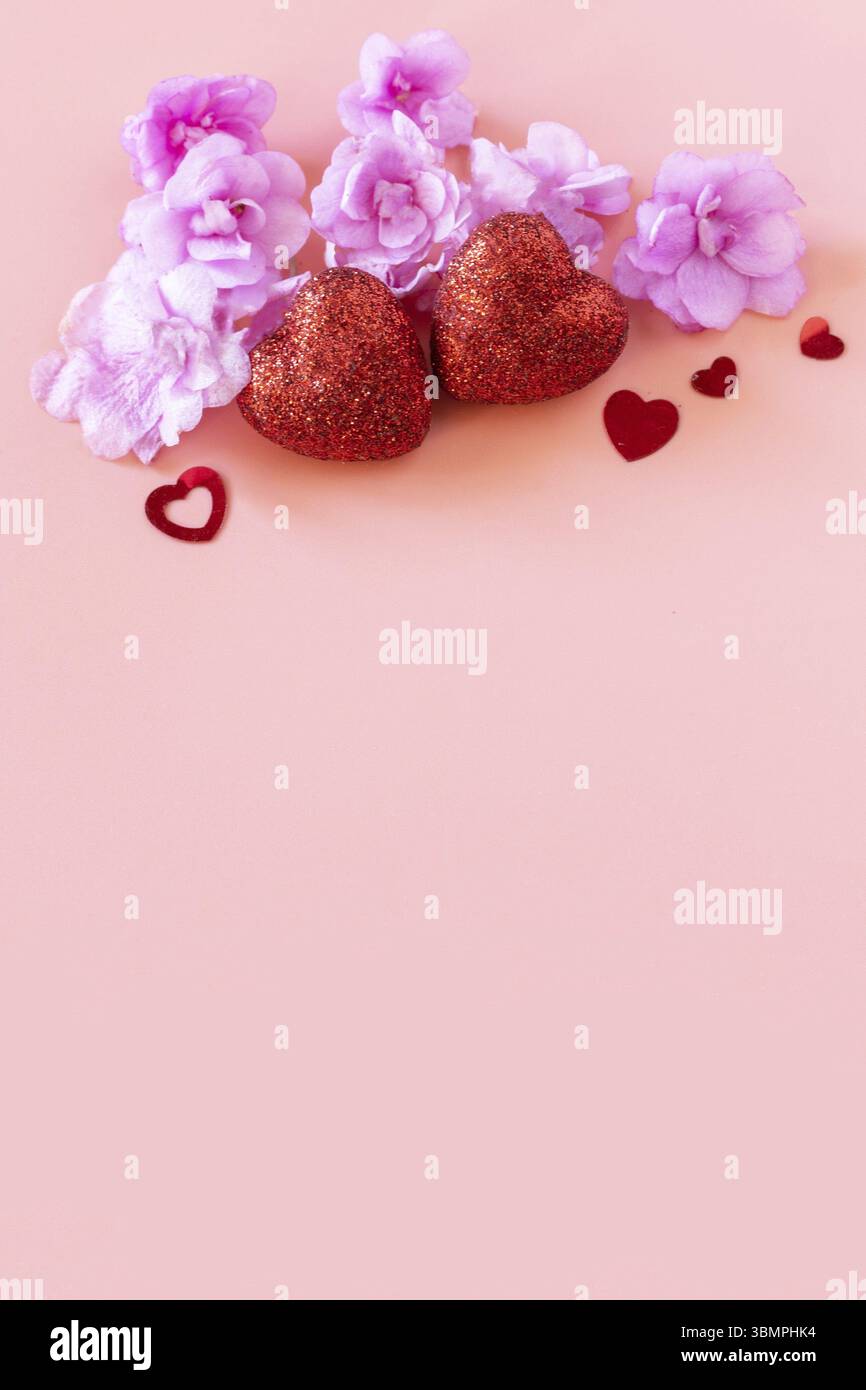 San Valentino, amore e nozze. Fiori lilla viola e cuori rossi su sfondo rosa. Disposizione piatta, vista dall'alto. Copia spazio Foto Stock