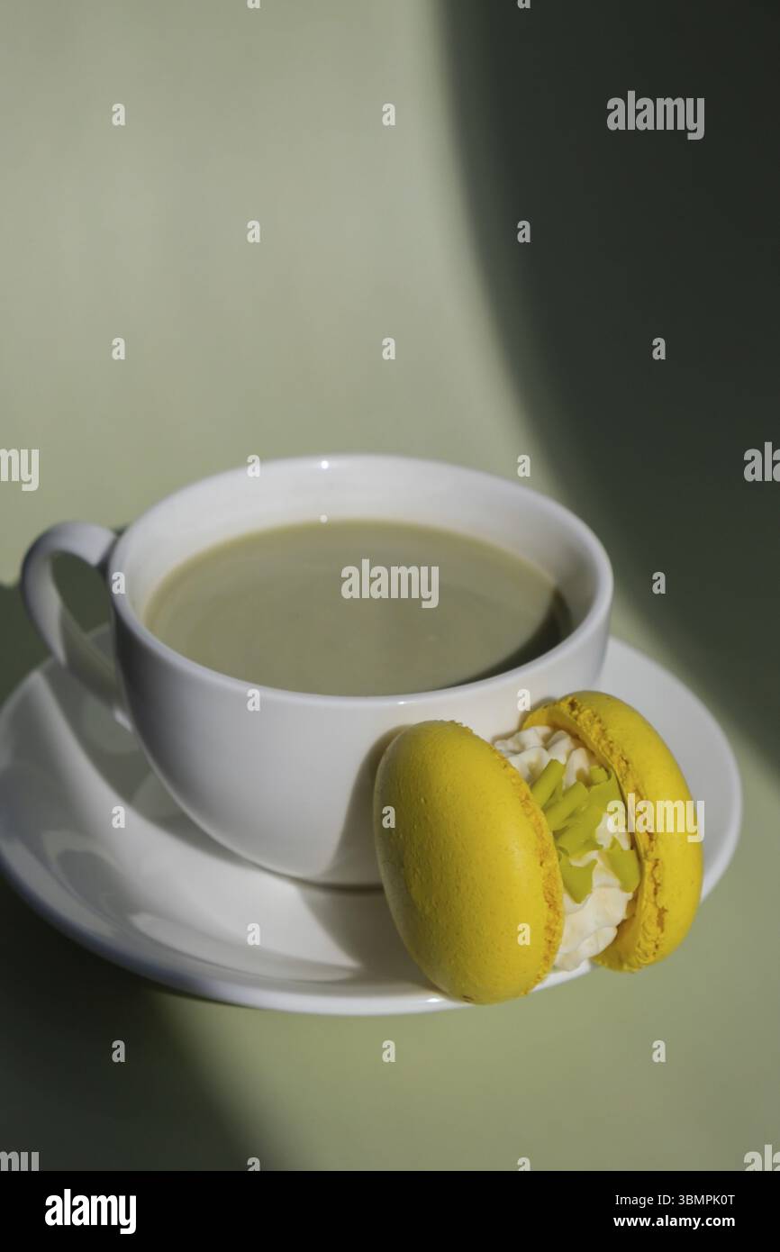 Latte matcha verde con dessert di macaron giallo su sfondo pastello con ombre profonde e creative. Concetto di colazione natalizia tè mattutino e bevanda. Accogliente Foto Stock
