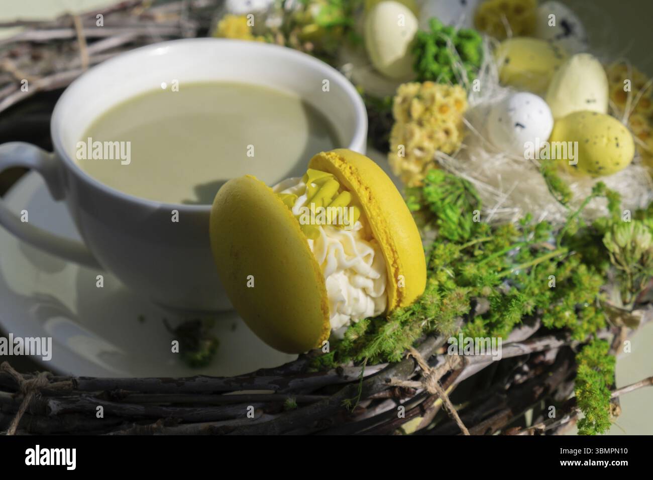 Decorazione della corona di uovo di Pasqua dolce di macaron dolce tazza di tè matcha a base di piante verdi latte in un'atmosfera accogliente al mattino. Romanticismo creativo per le vacanze Foto Stock