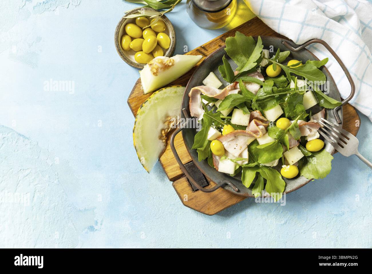 Antipasto tradizionale spagnolo e italiano. Insalata mediterranea estiva con melone, pancetta, olive, formaggio bianco e rucola su fondo di pietra blu. Vi Foto Stock