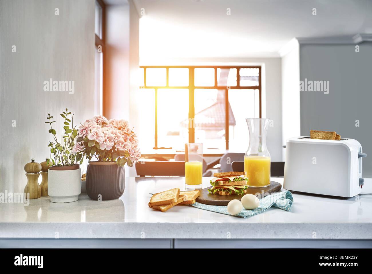 Bianco elettrico pane tostapane con succo di arancia a sandwich con sul tavolo da cucina. La prima colazione nell'accogliente cucina. Utile e il cibo gustoso. Sun flare Foto Stock