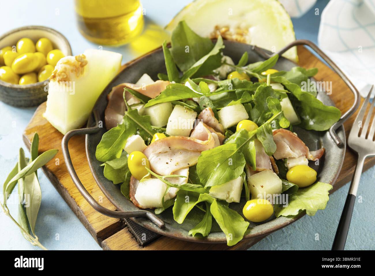Antipasto tradizionale spagnolo e italiano. Insalata mediterranea estiva con melone, pancetta, olive, formaggio bianco e rucola su sfondo di pietra blu Foto Stock