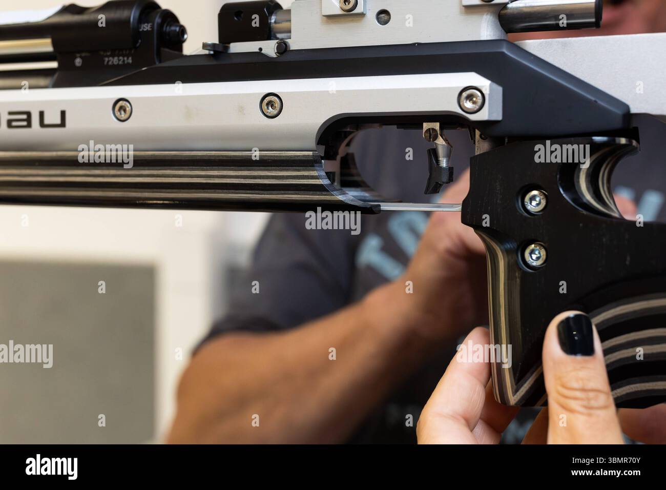 Landkreis Osnabrück, Deutschland 25. Giu 2025: Im Bild: Eine Nahaufnahme zeigt den hochpräzisen Abzugsmechanismus eines Sportgewehrs, wahrscheinlich eines Luftgewehrs, das von einer person mit sorgfältiger Handhabung gehalten wird. Der Fokus liegt auf den feinen Justiermöglichkeiten und der komplexen Mechanik des Abzugs, der Schussauslösung die für im Präzisionsschießsport entscheidend ist. Man erkennt die fein gearbeiteten Metallteile und Schrauben, die eine individuelle Einstein des Abzugswiderstands und des Vorwegs ermöglichen. Die Person, Die das Gewehr hält, trägt dunklen Nagellack, W Foto Stock