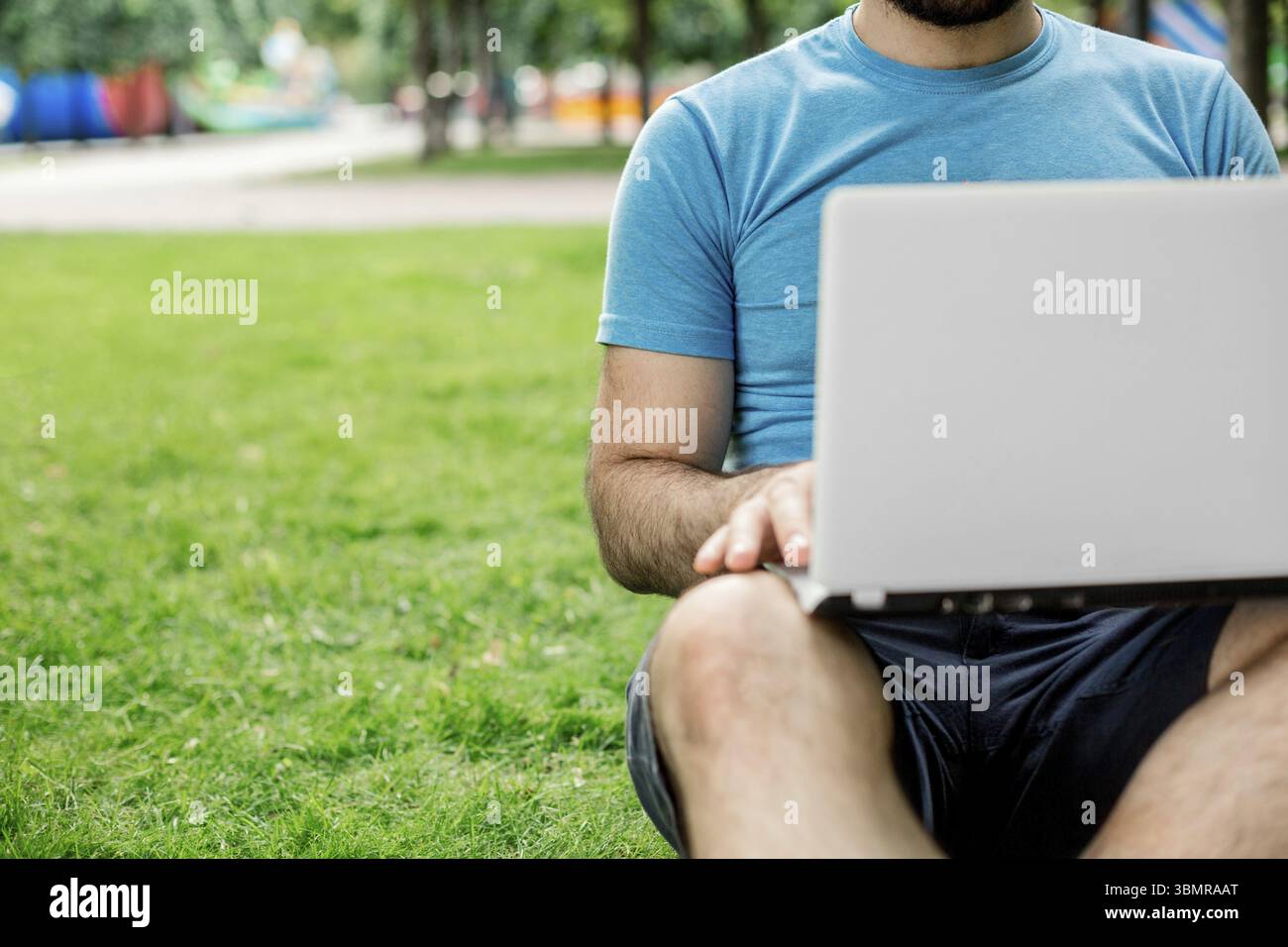 Giovane uomo che usa e digita un computer portatile nell'erba estiva. Libero professionista che lavora nel parco all'aperto Foto Stock