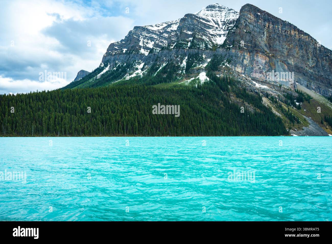 Lago alpino turchese di fronte a massicce montagne innevate e foresta sempreverde Foto Stock