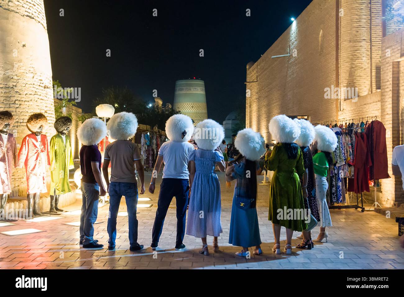 Khiva, Uzbekistan - 12 luglio 2024: Turisti che provano i tradizionali cappelli uzbeki a Khiva, Uzbekistan. Persone viste da dietro esplorando la cultura locale in un ciao Foto Stock