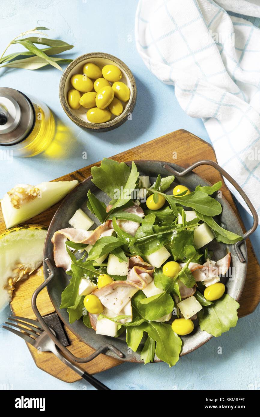 Antipasto tradizionale spagnolo e italiano. Insalata mediterranea estiva con melone, pancetta, olive, formaggio bianco e rucola su fondo di pietra blu. Vi Foto Stock
