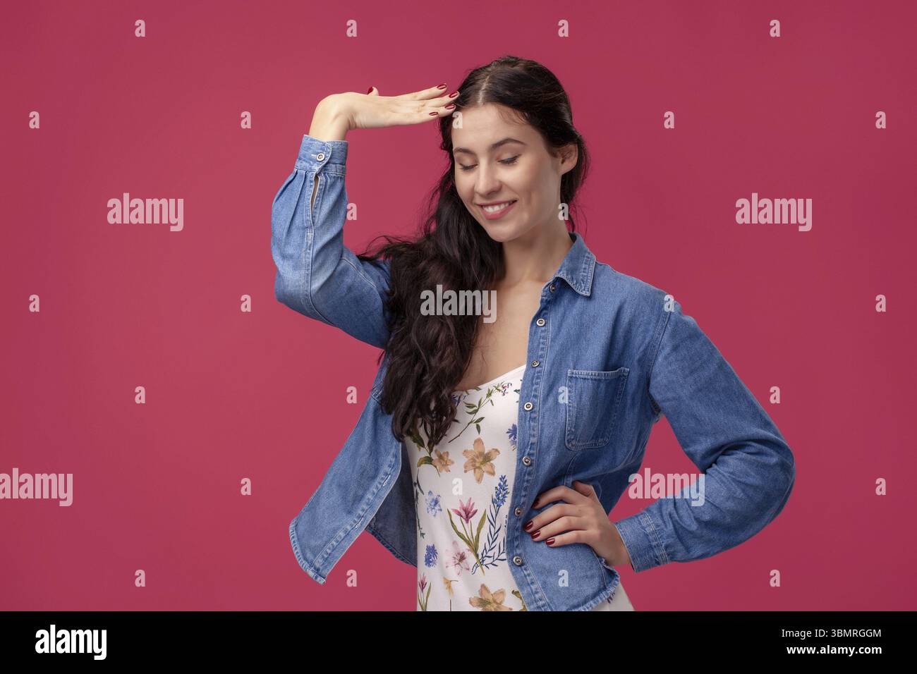 Ritratto di una giovane donna allegra in un abito bianco con stampa floreale e camicia in denim blu su uno sfondo rosa della parete in studio. Lei è peccato Foto Stock