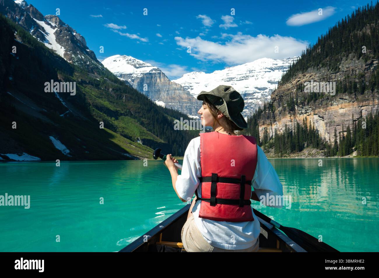 Persona che pagaia in canoa su un lago turchese con spettacolare sfondo innevato di montagna e scogliere boscose Foto Stock