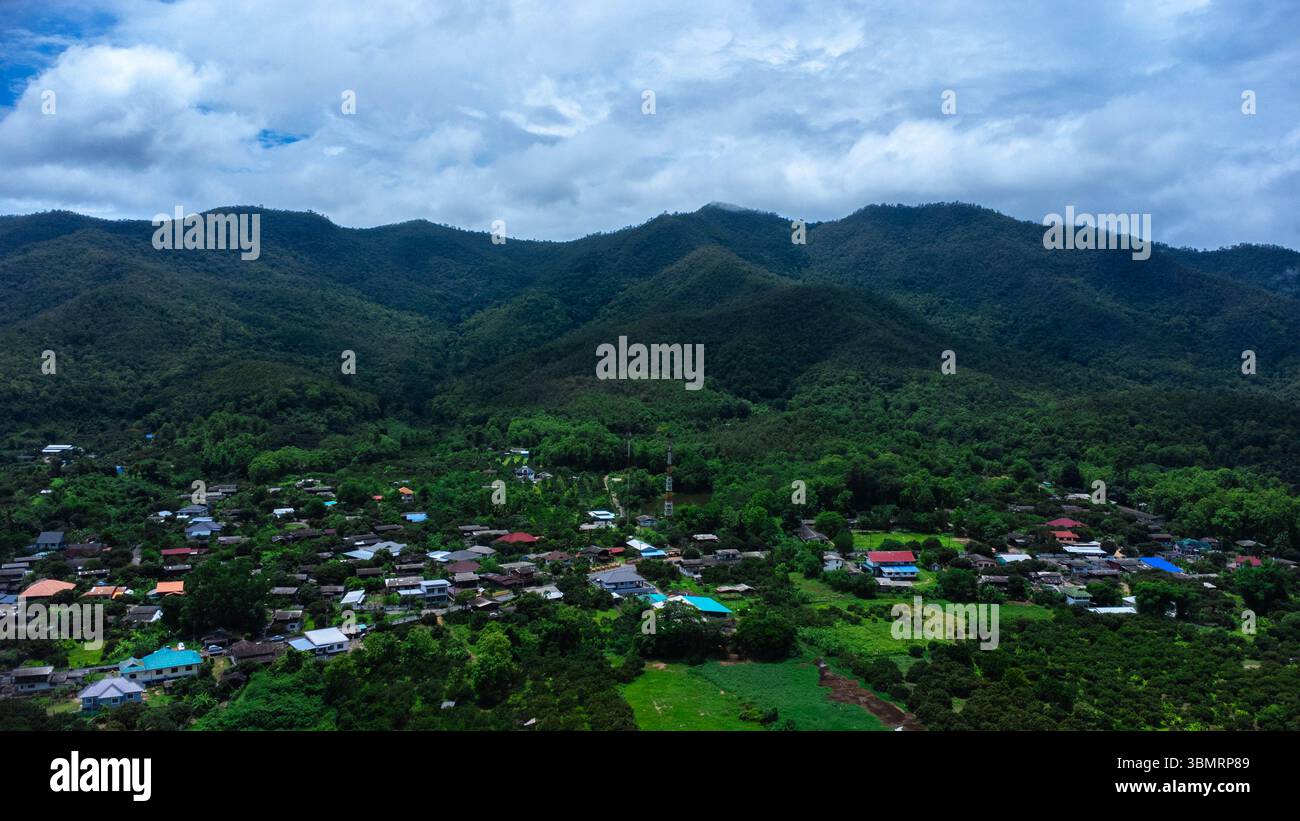 Paesaggio di stagione delle piogge di un villaggio di montagna al mattino e montagne sullo sfondo. Foto Stock
