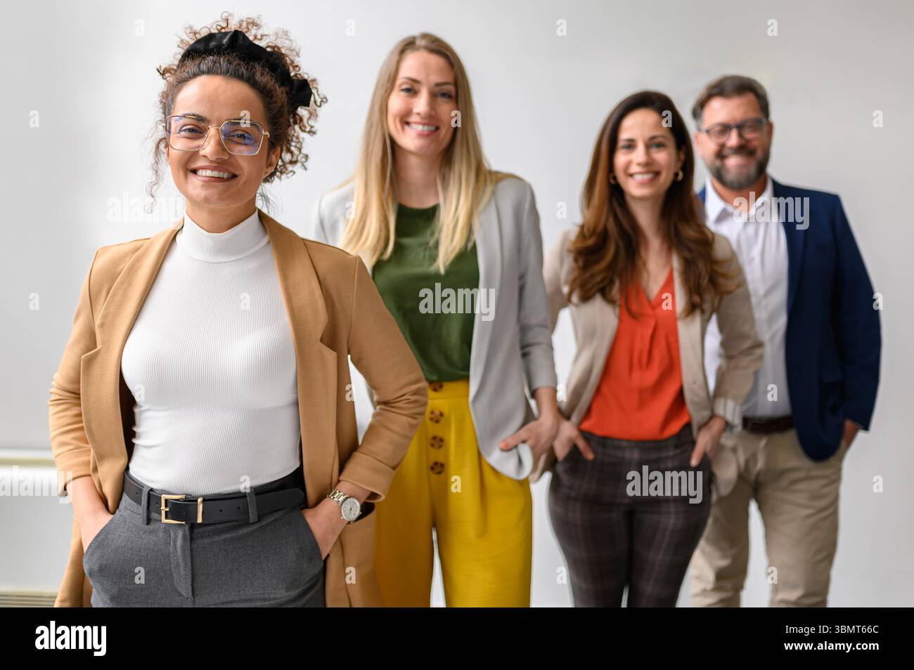 Ritratto di un team di professionisti sorridenti con le mani in tasca che posano insieme in fila su sfondo bianco Foto Stock