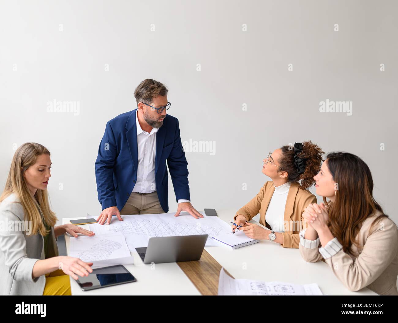 Architetto maschile con progetti e computer sul tavolo che spiegano piani e progetti alle colleghe in riunione Foto Stock