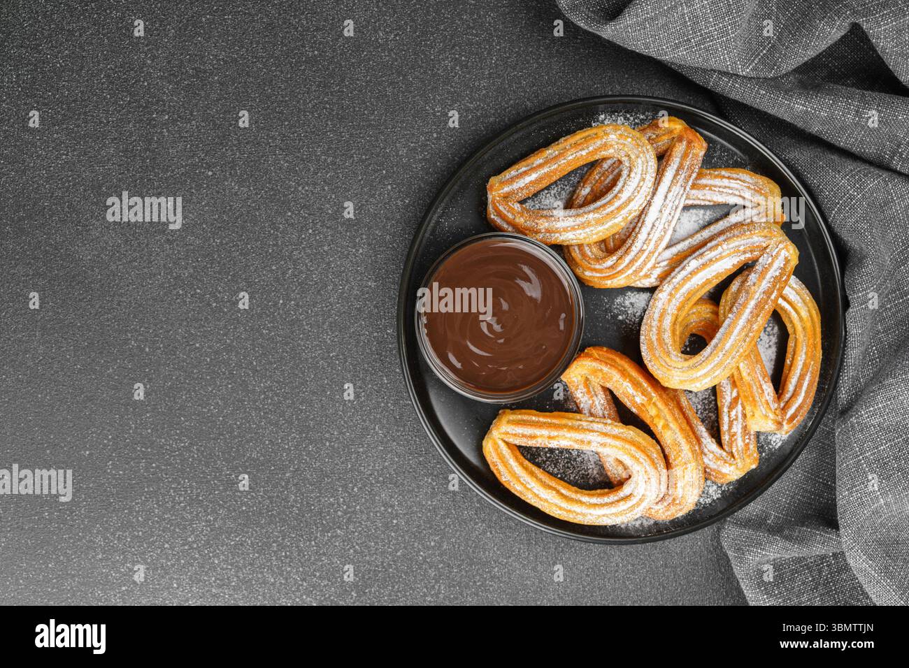 Tradizionale churros da dessert spagnolo, pasta fritta spolverata con zucchero a velo e salsa al cioccolato su sfondo nero. Street food, snack dolci, Foto Stock