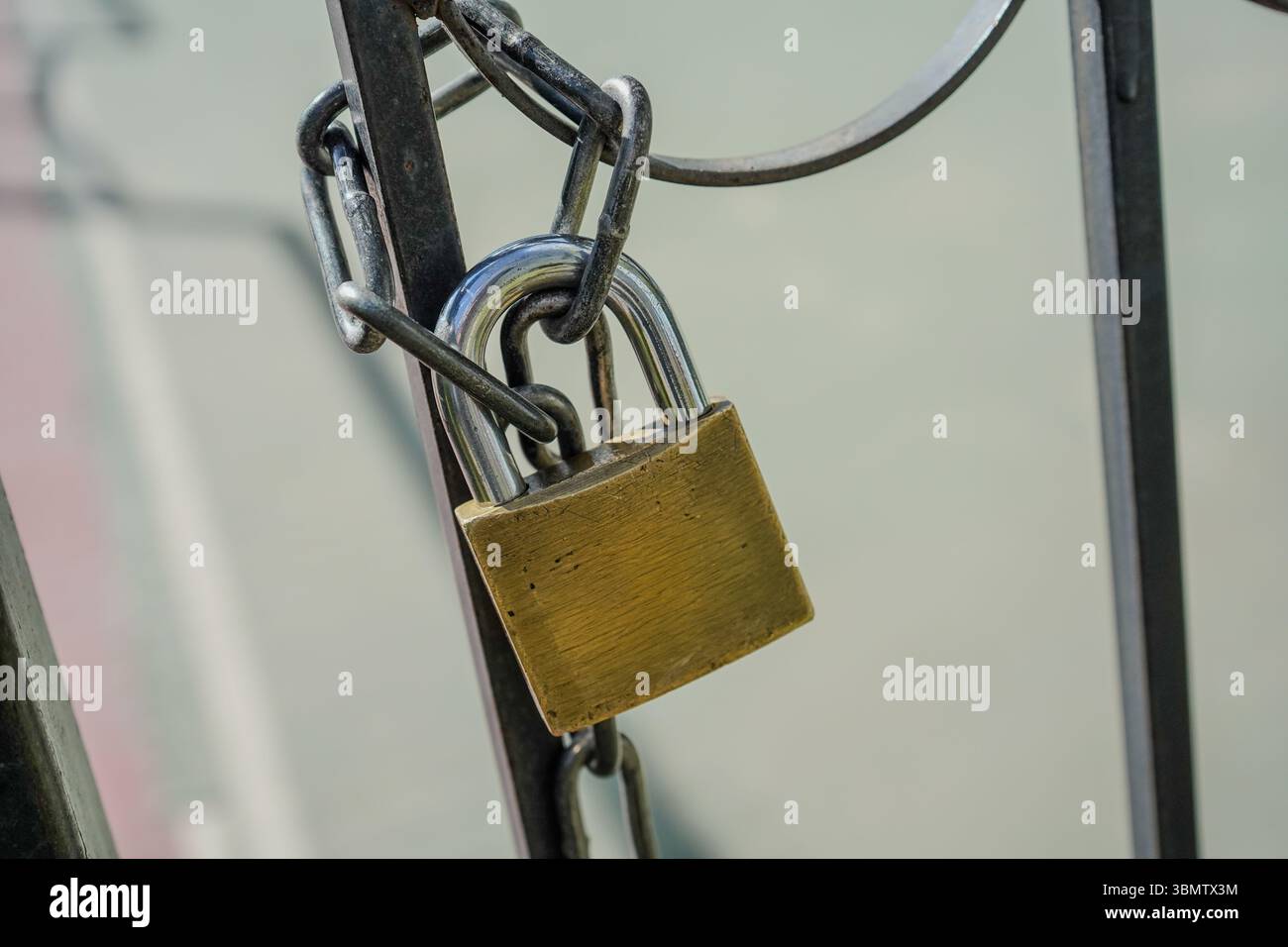 Vista ravvicinata di un lucchetto fissato a una catena avvolta intorno a un telaio in metallo. La catena è composta da maglie spesse di colore scuro. Foto Stock