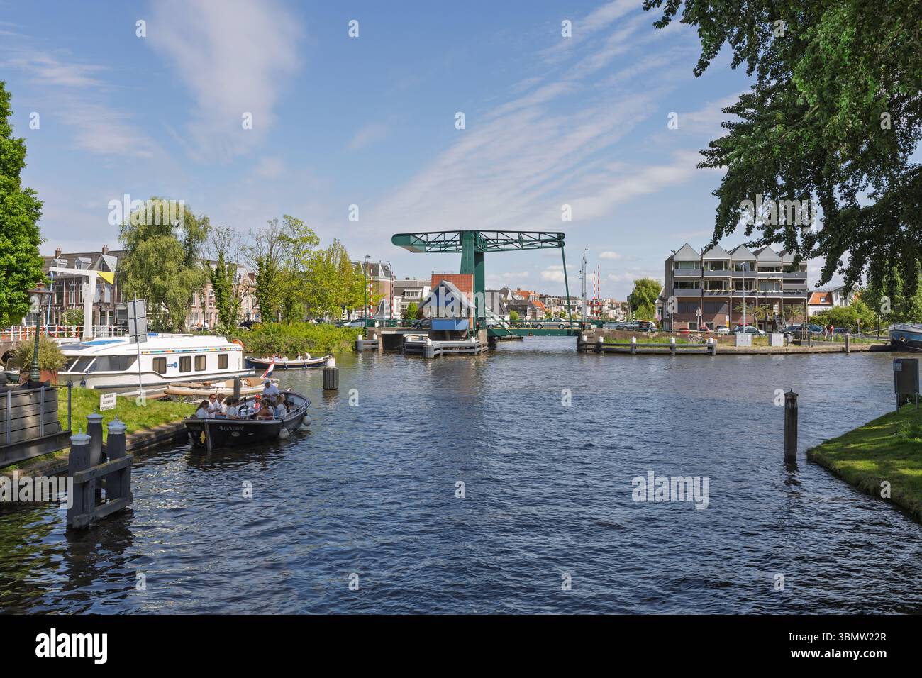 Pittoresca vista sul canale di Leida, Paesi Bassi, con un classico ponte levatoio verde, barche e un'affascinante architettura sul mare sotto un cielo blu. Leid Foto Stock
