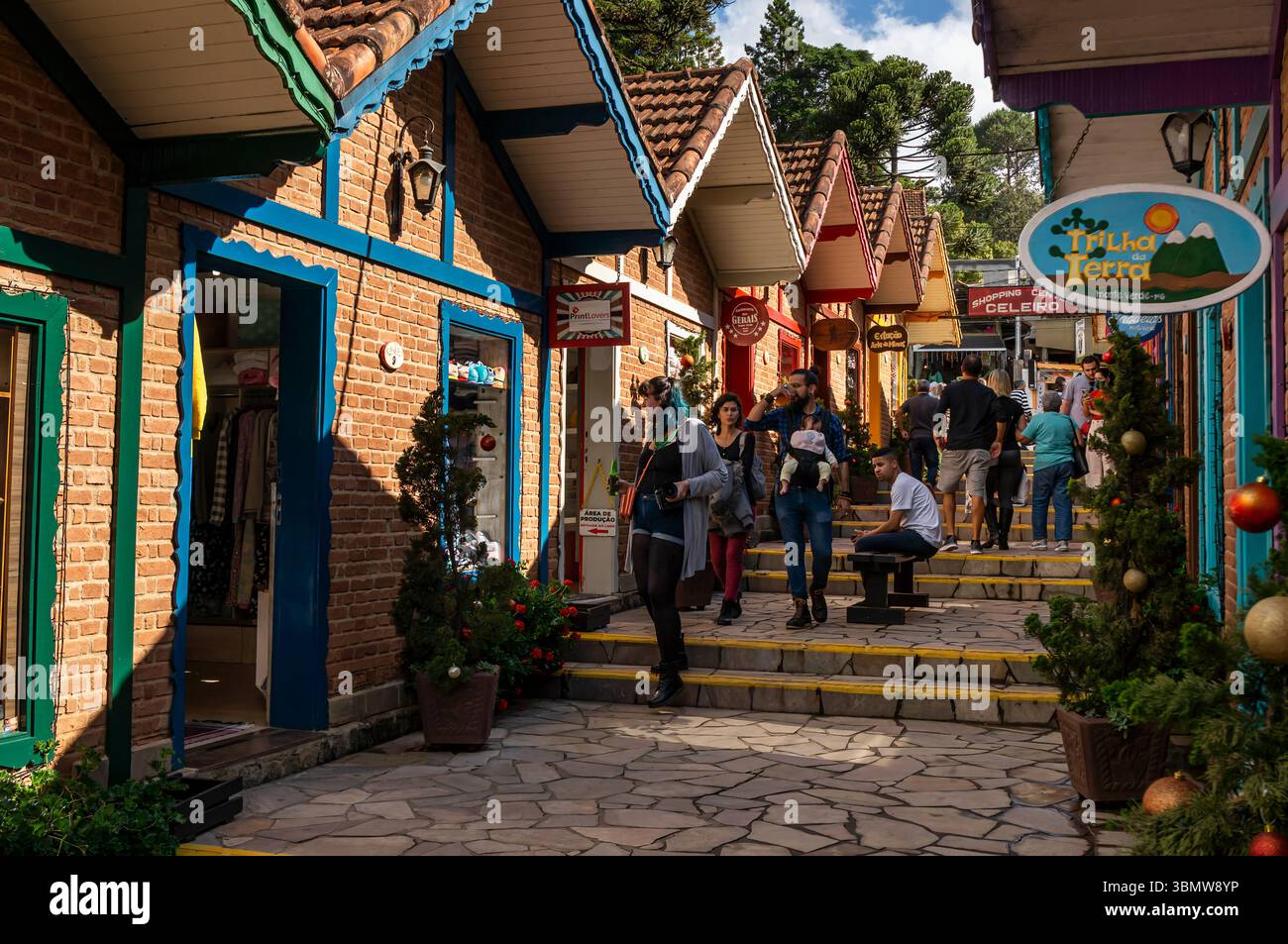 Gli amanti dello shopping salgono le scale nel festoso vicolo alpino del centro commerciale Celeiro, fiancheggiato da negozi di mattoni e alberi di Natale in una giornata di sole. Foto Stock