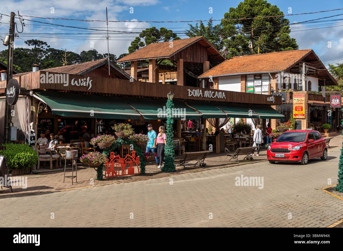 Una Ford Ka rossa passa accanto al ristorante Dona Mucama in Monte Verde avenue, con pedoni a piedi e posti a sedere all'aperto sotto il cielo soleggiato. Foto Stock