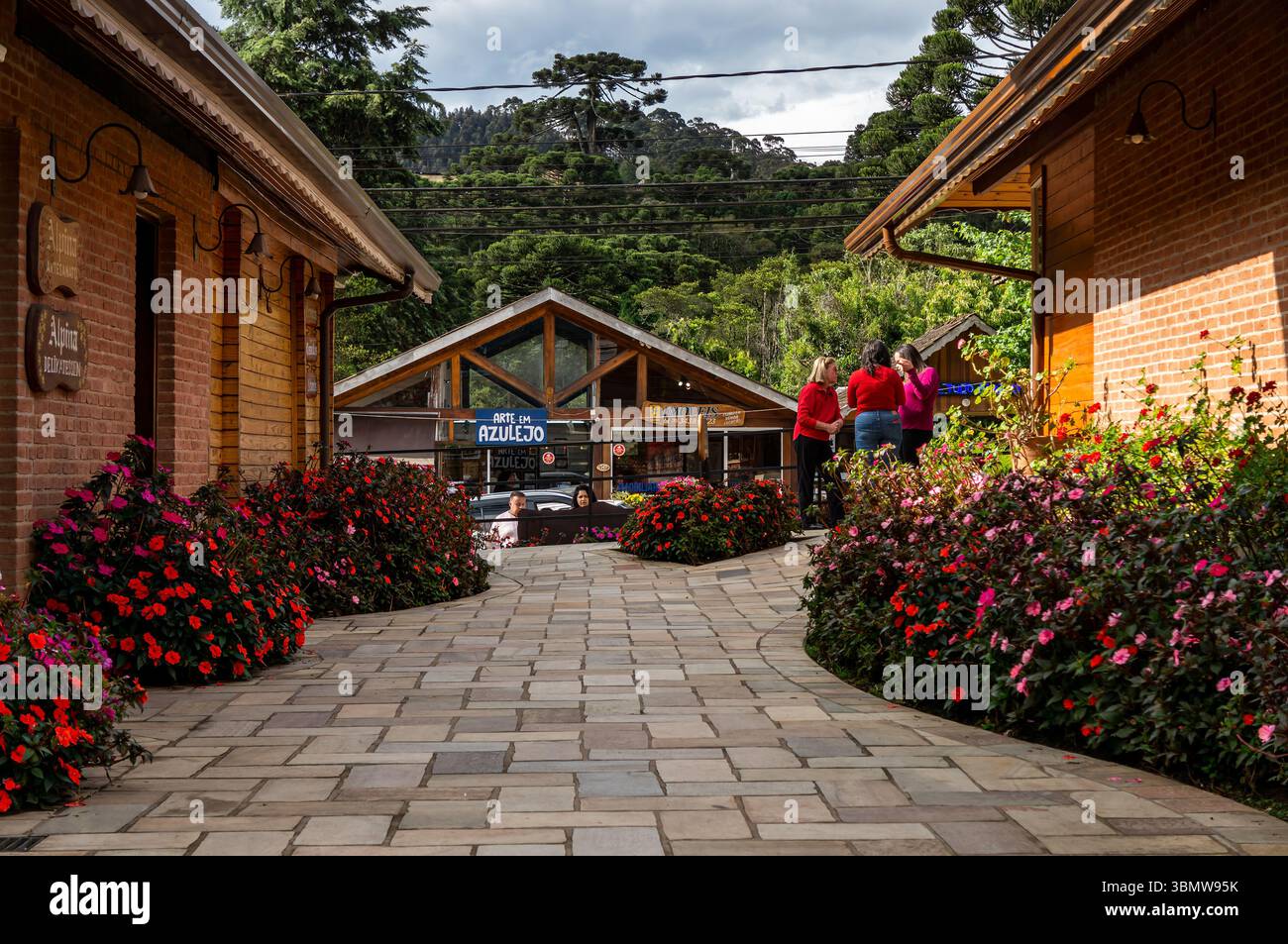 Le donne chiacchierano sul sentiero in mattoni fiancheggiato da fiori vicino ai negozi di Alpina e Arte em Azulejo in viale Monte Verde, con verdi colline boscose sullo sfondo. Foto Stock