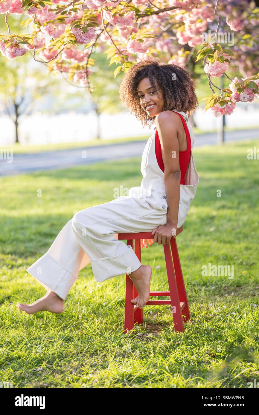 Una giovane donna afroamericana con capelli ricci sorride alla telecamera. Foto Stock