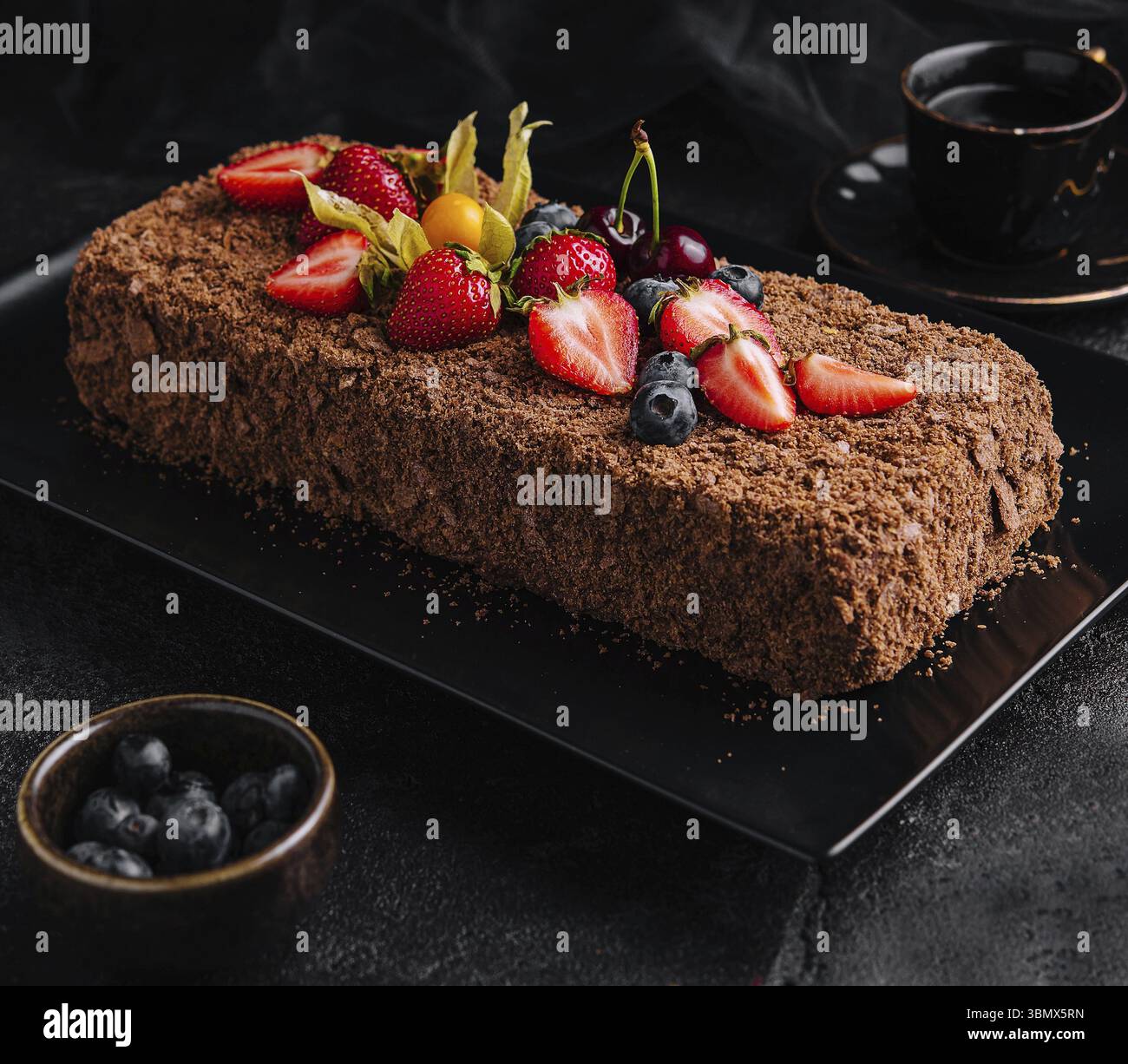 Natura morta del cibo, torta Napoleone al cioccolato con frutti di bosco su un piatto di pietra Foto Stock