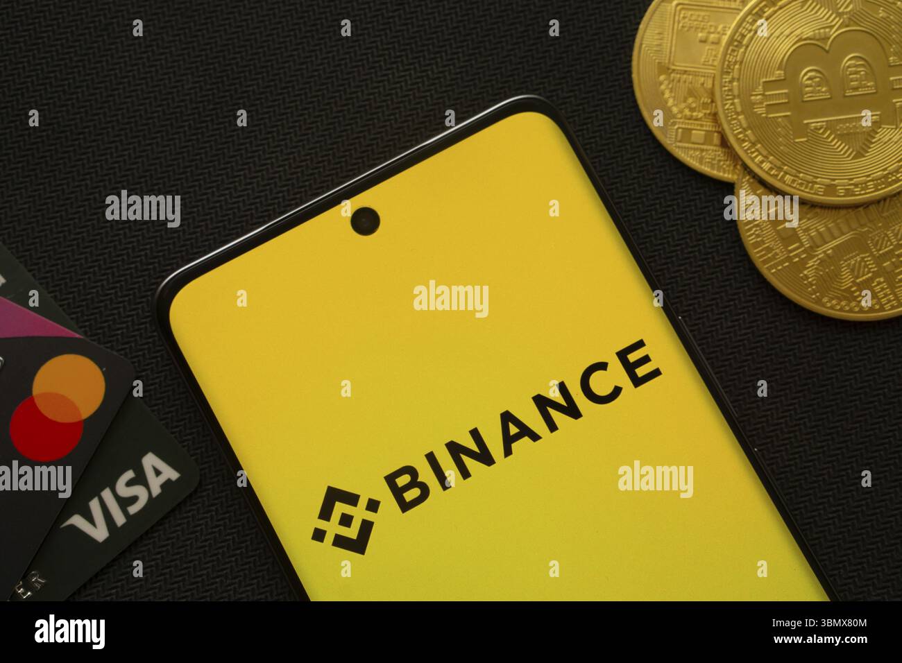 Dhaka, Bangladesh - 22 giugno 2025: Smartphone con logo Binance circondato da monete e carte di pagamento Bitcoin Foto Stock