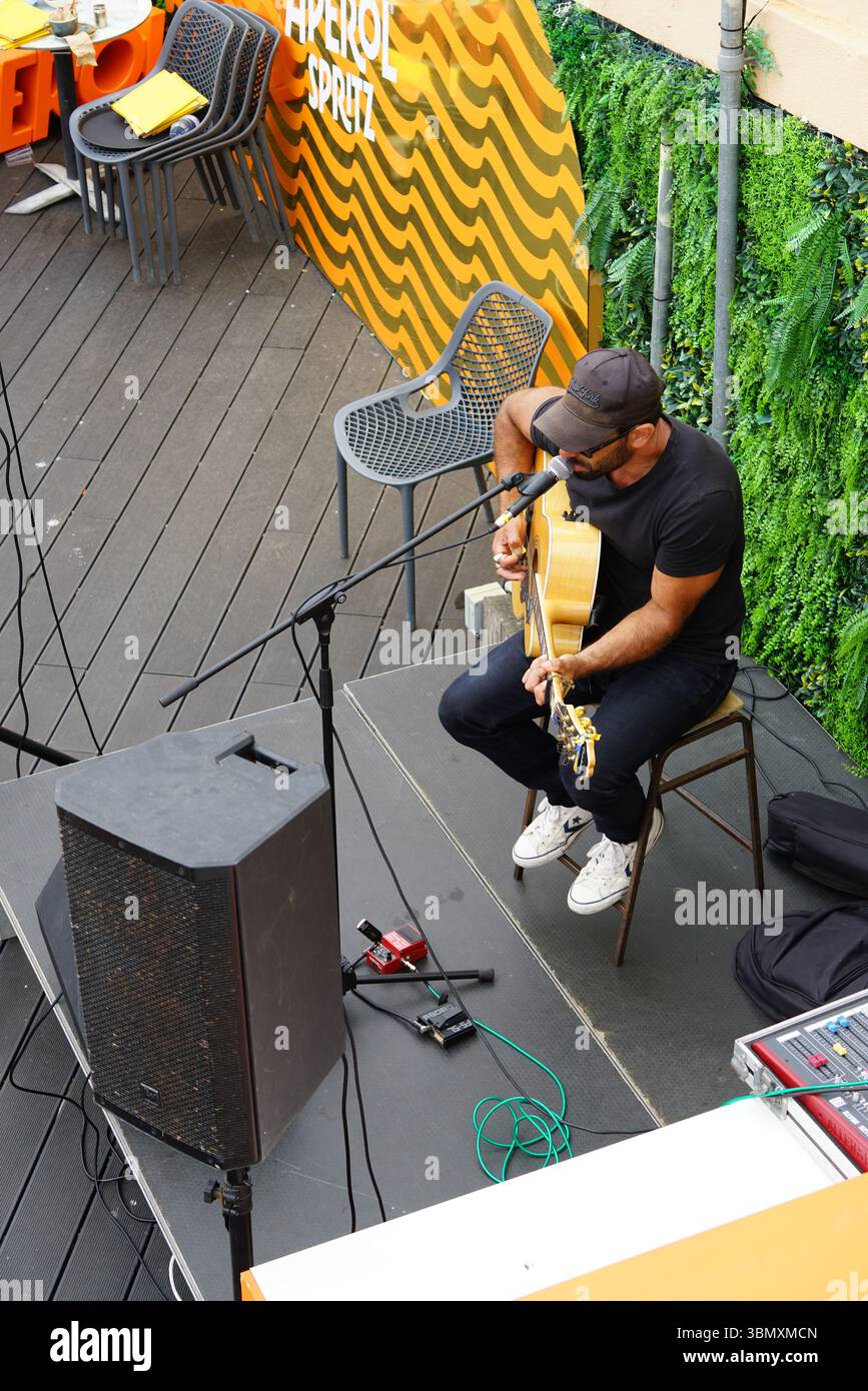Musician Performing Acoustic Guitar all'aperto presso l'elegante Urban Cafe Venue. Brighton, Inghilterra Foto Stock