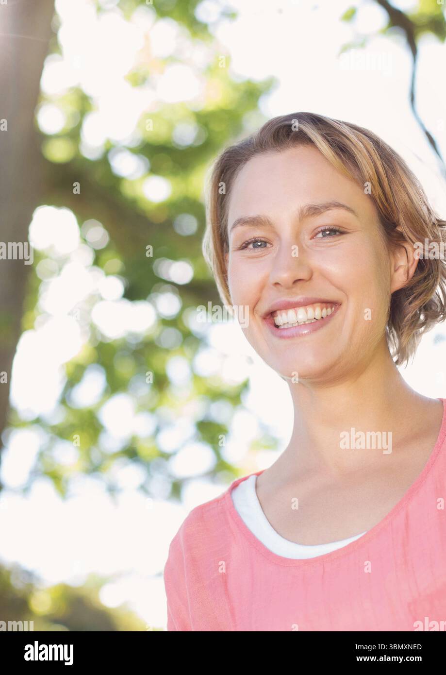 Ritratto di una giovane donna sorridente contro l'albero Foto Stock