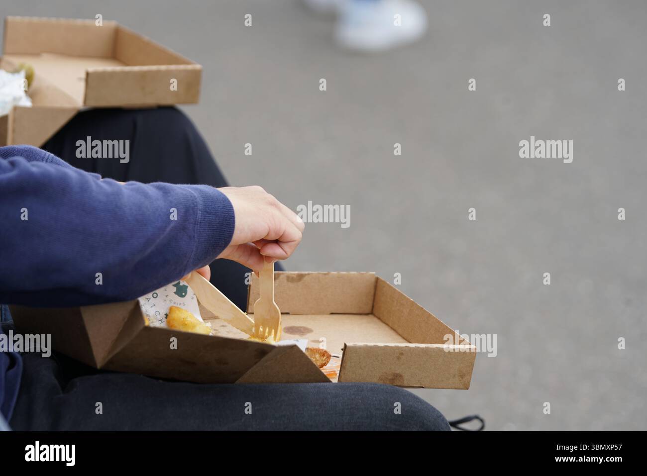 Persona che mangia un pasto da asporto all'aperto utilizzando utensili ecologici. Brighton, Inghilterra Foto Stock
