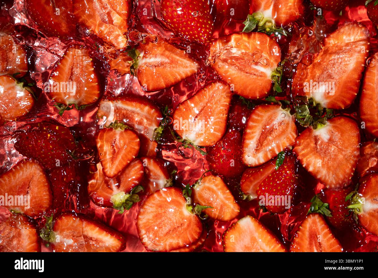 Fragole cadute in acqua. Effetto Splash e look estivo vivace. Foto Stock
