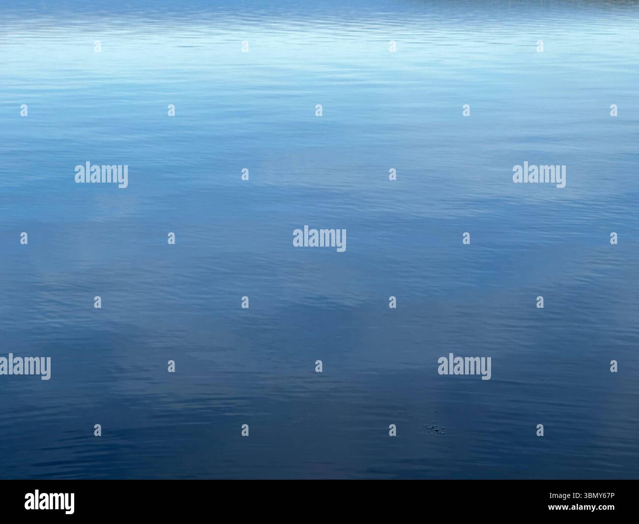 Il tranquillo oceano si estende verso l'orizzonte, riflettendo il cielo blu e le morbide nuvole sopra. Foto Stock