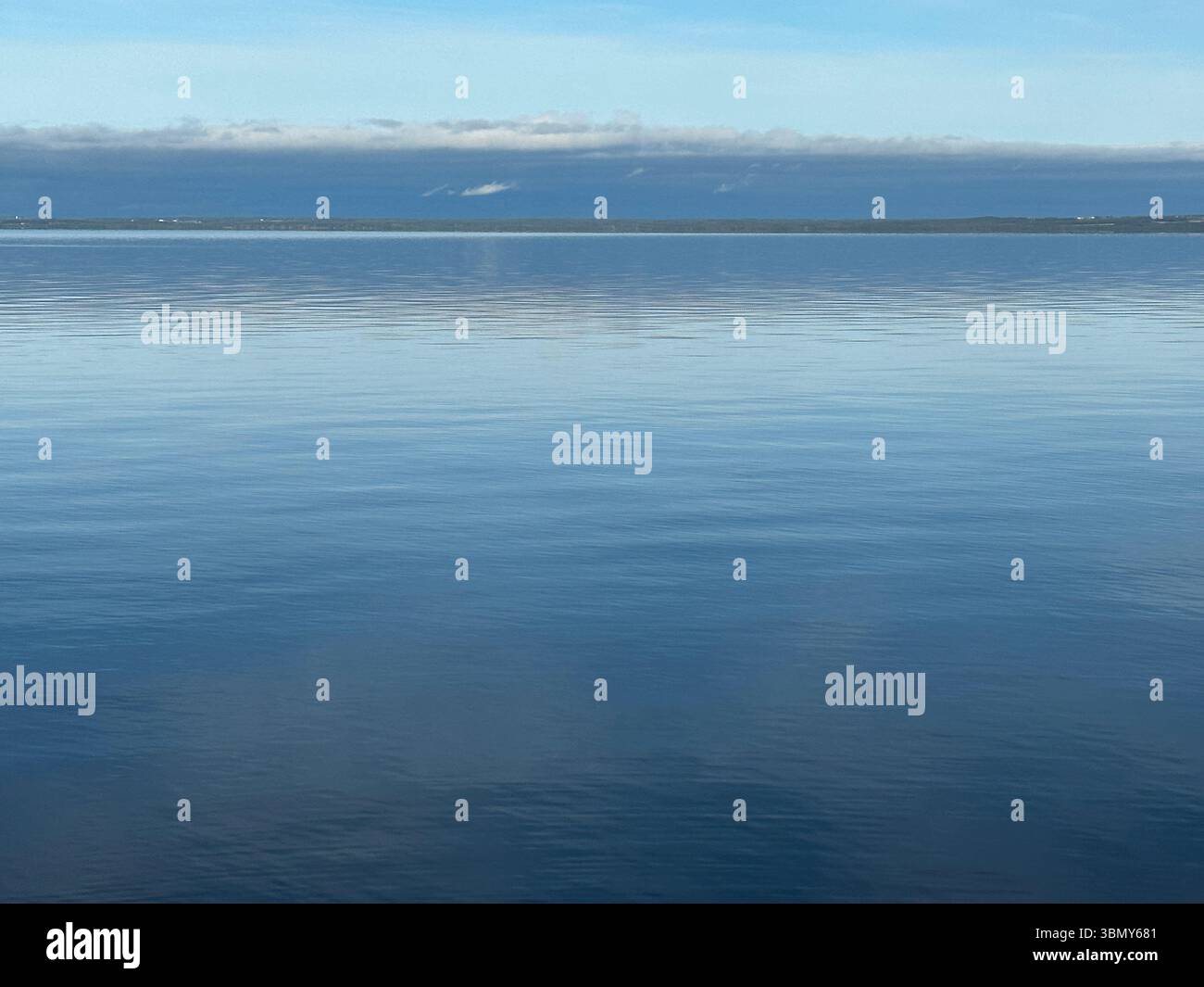 Il tranquillo oceano si estende verso l'orizzonte, riflettendo il cielo blu e le morbide nuvole sopra. Foto Stock