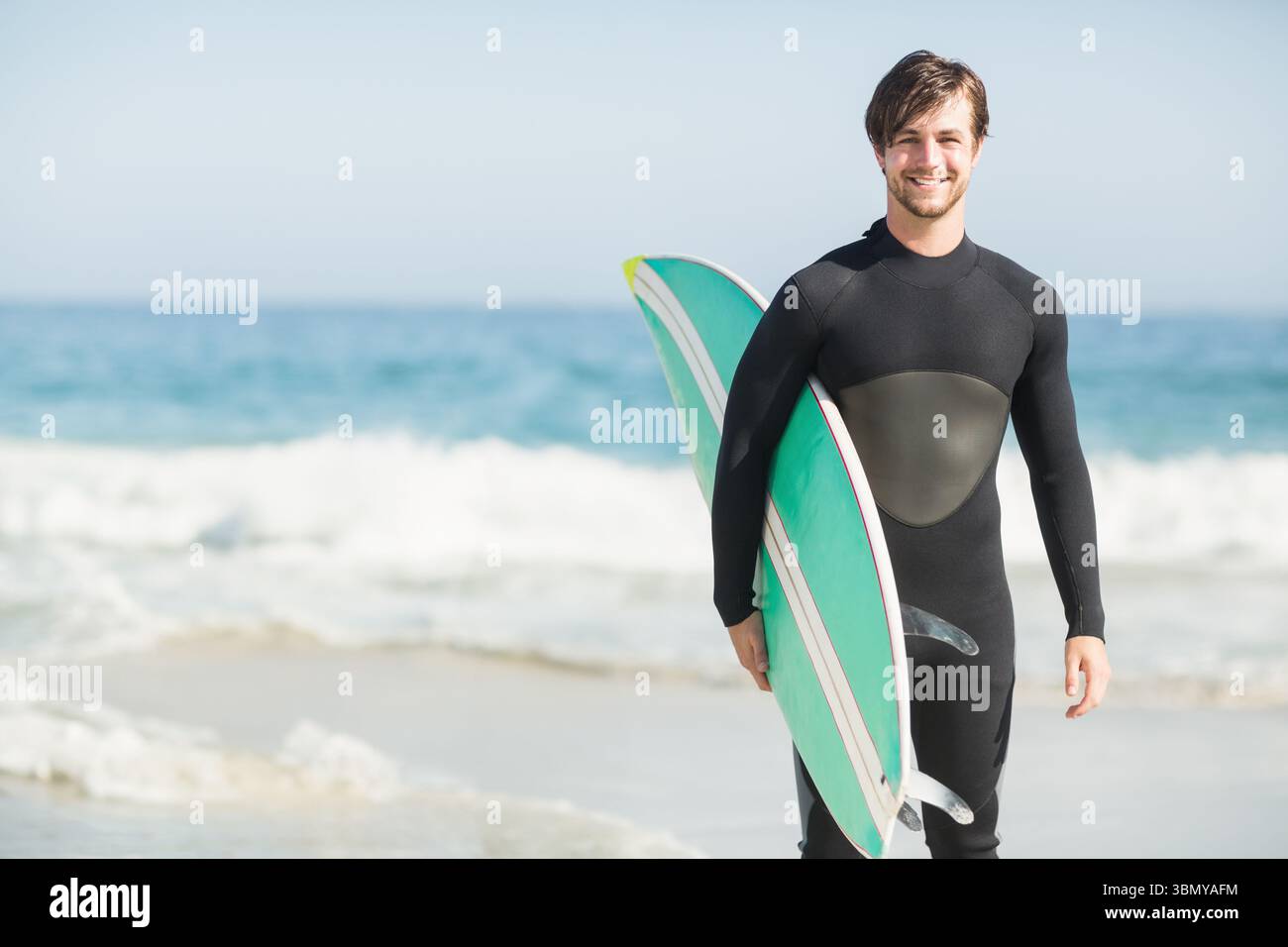 Surfista maschile che emerge dalle onde in spiaggia indossando muta con tavola da surf verde-bianca, spazio copia Foto Stock